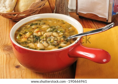 A bowl of healthy kale and white bean soup with dinner rolls