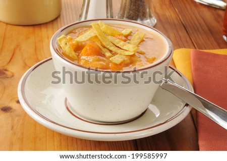 A cup of chicken tortilla soup on a rustic wooden table