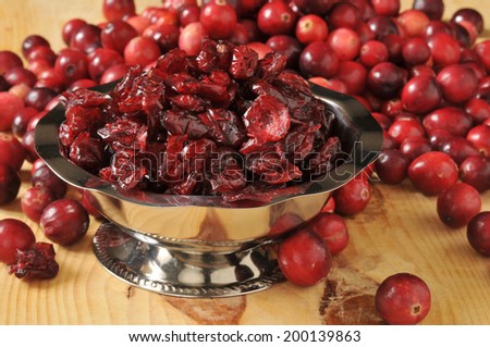 A silver bowl of dried cranberries with fresh cranberries in the background