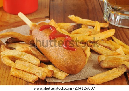 a corn dog and french fries with beer on a rustic wooden bar counter
