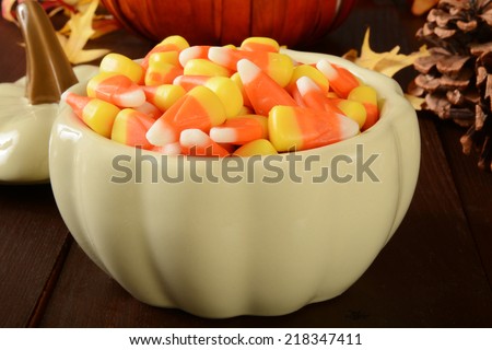 A pumpkin shaped dish of candy corn on a Halloween or Thanksgiving dinner table