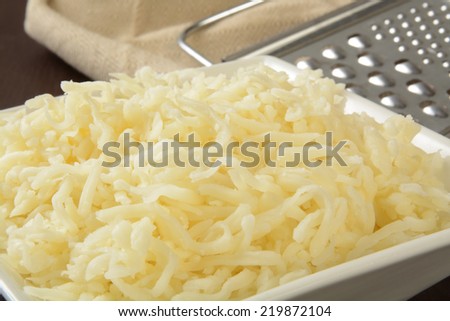 A bowl of shredded mozzarella cheese with a grater in the background