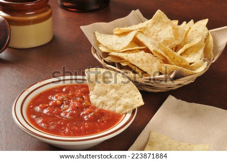 Corn tortilla chips with salsa and a bottle of beer in the background