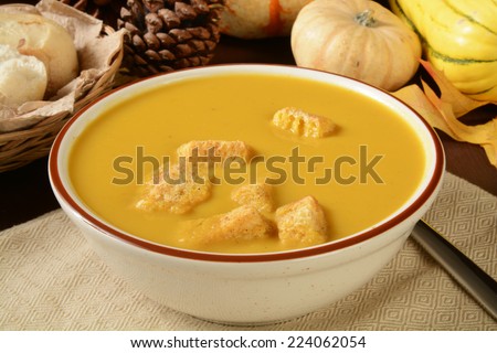 A bowl of butternut squash soup with croutons and dinner rolls