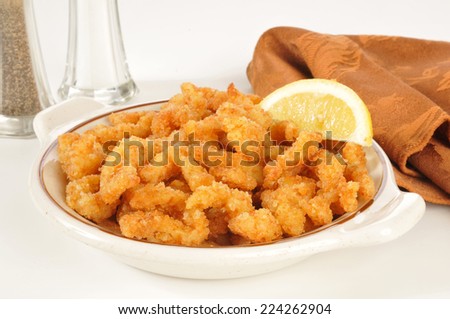 A bowl of breaded deep fried clams with a wedge of lemon