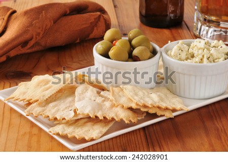 Flatbread crackers with green olives and feta cheese on a bar counter with beer