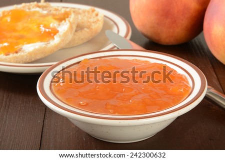 a bowl of peach jam with English muffins in the background, shallow depth of field, focus on jam