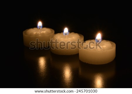 Three tea light candles burning on a dark table