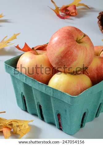A container of ripe gala apples on a table with autumn leaves