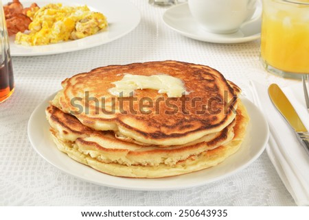 A stack of home made pancakes with scrambled eggs and bacon