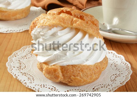 A large golden cream puff on a doily with a cup of coffee