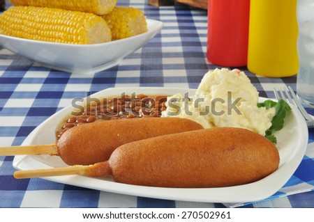 Corn dogs with mashed potatoes and baked beans on a picnic table