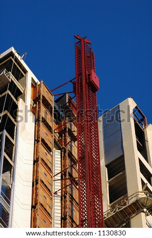 A construction elevator rises up the side of a hi-rise being built