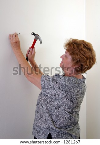A woman hammers a nail in a wall