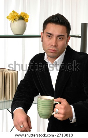 A young man leaning on a book shelf and drinking coffee or tea