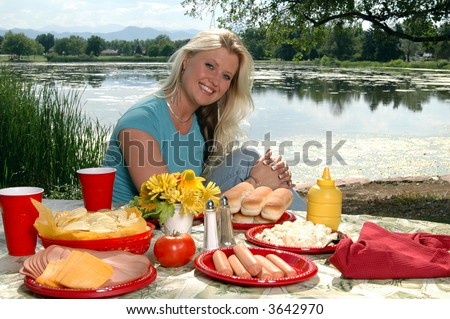 A beautiful blond woman sitting at a picnic table by a lake
