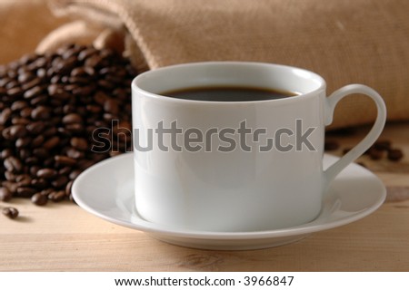 Coffee spills out of a burlap bag behind a fresh cup