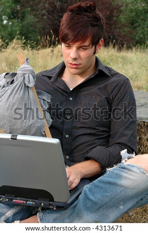 A young man with a knapsack working on a computer in the wilderness