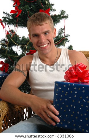 A happy young man holding a Christmas present in front of the tree