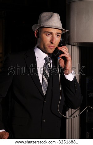 A man in a suit and hat making a call from a pay phone, sepia toned