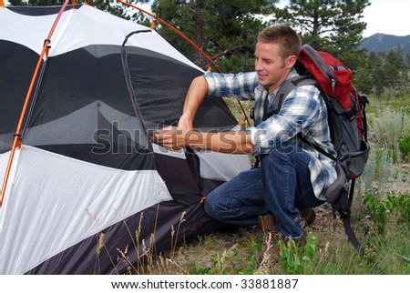A man in a backpack zipping up a tent