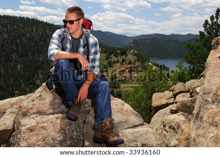 A backpacker sits on top of a mountain above a lake