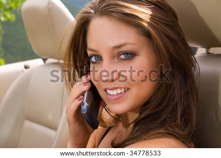 A beautiful woman in a sports car talking on a cell phone.