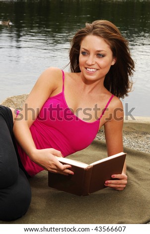 A beautiful woman reading a book by a mountain lake