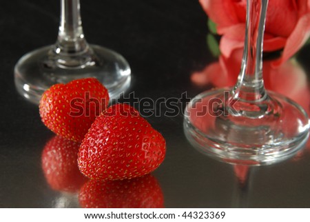 A red rose and strawberries with wine glasses on a glass table, suggesting romance or Valentine\'s Day