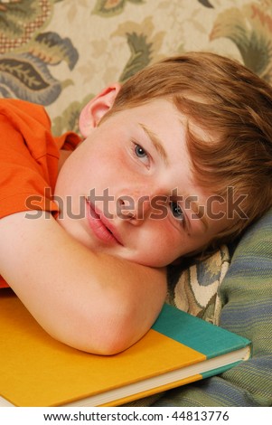 A sleepy boy resting his head on a school book