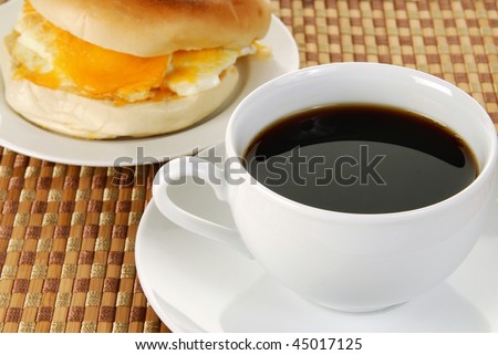 A cup of black coffee and a bagel and egg sandwich