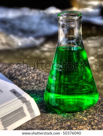 A laboratory flask and a text book beside a mountain stream suggesting eco science.  This is an HDR image.