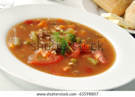 A bowl of vegetable beef soup garnished with a sprig of dill