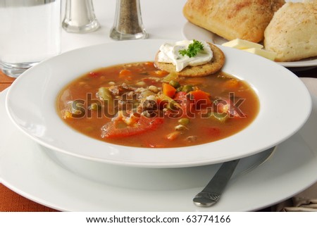 A bowl of delicious vegetable beef soup with rolls
