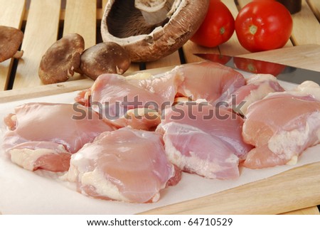 Raw chicken thighs, mushrooms and tomatoes on a cutting board