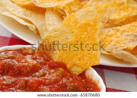 Close up shot of a tortilla chip with melted cheese in salsa - shallow depth of field, focus on the prominent chip