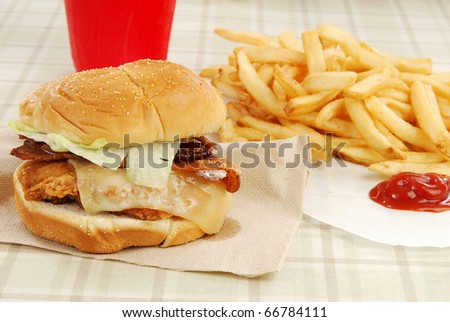 A chicken and bacon sandwich on a napkin with fries