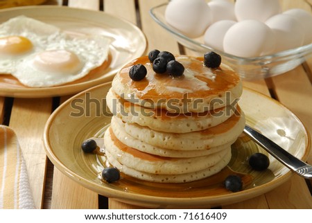 A stack of hotcakes with blueberries on top and a plate of sunny side up eggs