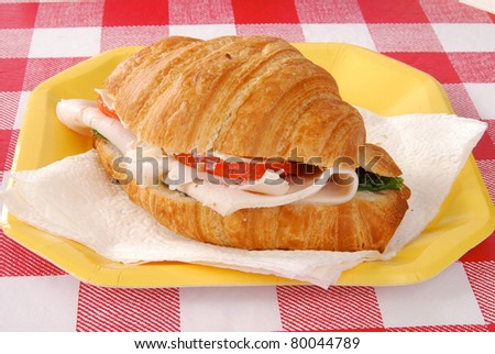 A fresh turkey croissant sandwich on a paper plate