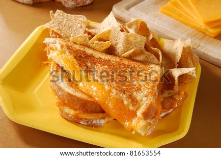 A grilled cheese sandwich on a paper plate and multigrain chips