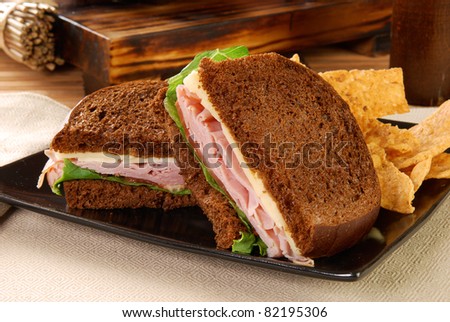 A ham and cheese sandwich on dark rye with tortilla chips