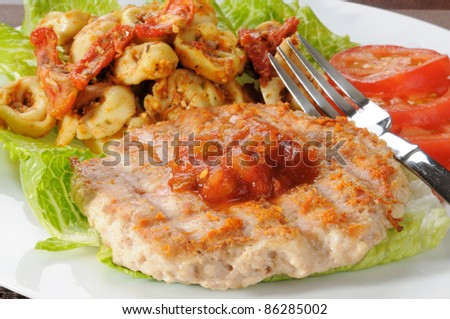 A grilled ground chicken or turkey patty with tortellini and roasted tomato pesto
