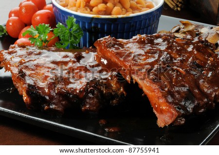 A closeup photo of baby back ribs drenched in barbecue sauce with baked beans