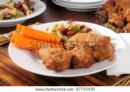 A snack plate at a party buffet loaded with chicken wings, carrot sticks and bean salad