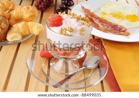 A breakfast feast with a yogurt parfait, bacon, eggs and croissants