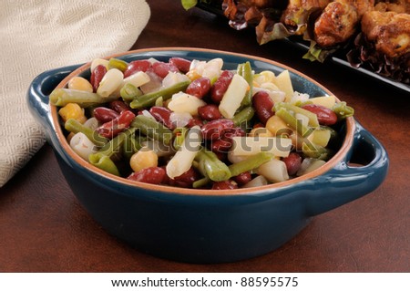 A bowl of four bean salad with chicken wings in the background