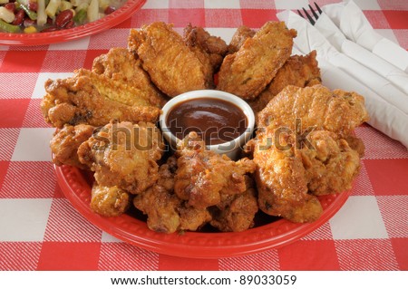 A plastic plate loaded with chicken wings and barbecue sauce on a picnic table