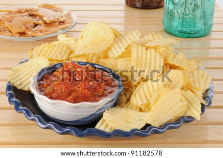 A party plate of chips and salsa with peanut brittle in the background