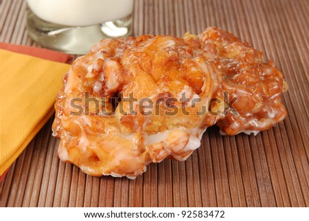 Two apple fritters on a placemat with milk