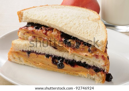 A peanut butter and strawberry jelly sandwich with an apple and milk